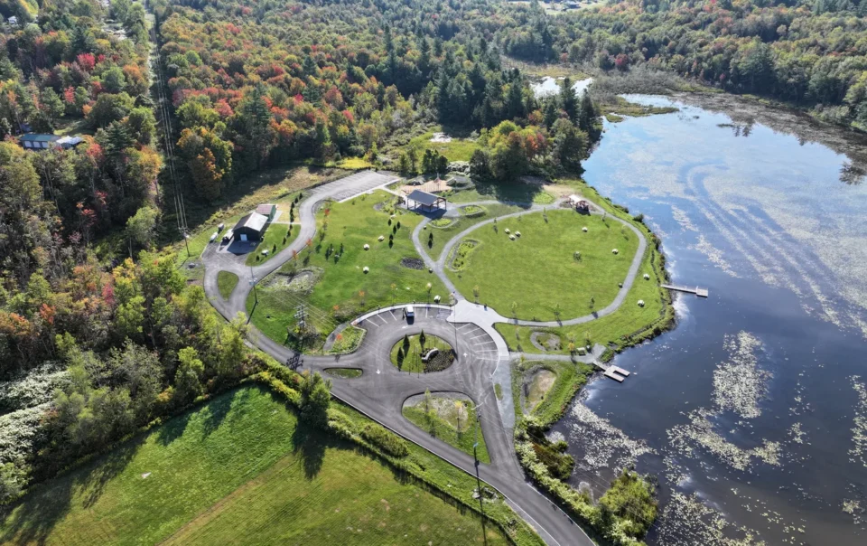 Aerial view of waterfront site design with curved pathways, green spaces, and buildings adjacent to forested landscape and