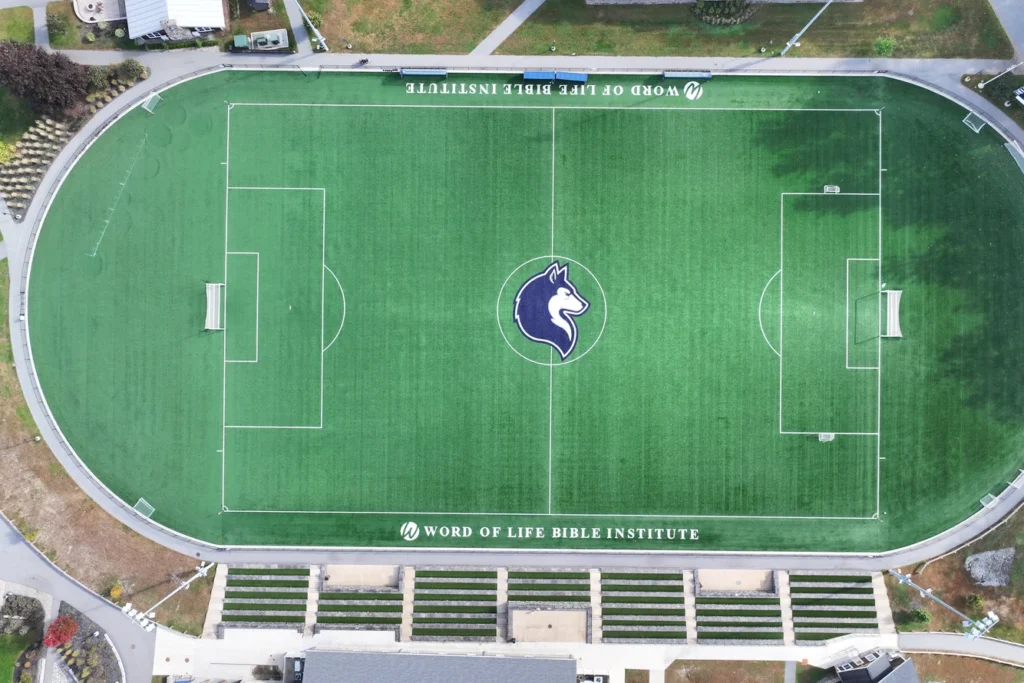 Aerial view of professional soccer field with blue horse logo, seating, and landscaped grounds at Word of Life Bible