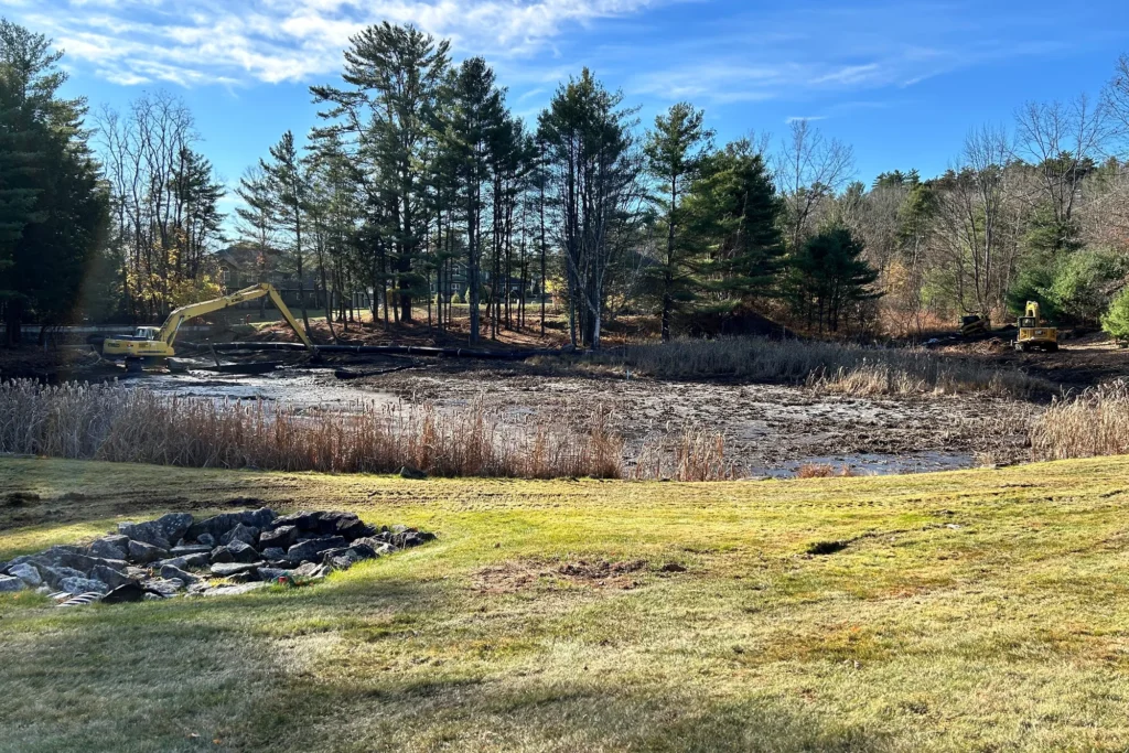 Wetland site design with excavation equipment, marsh vegetation, and stone erosion control along water edge.