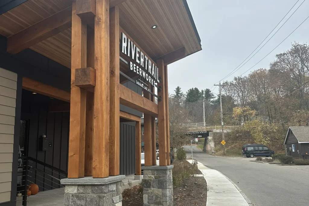River Trail Beerworks storefront with timber posts, stone base, and pedestrian walkway along Northeast community corridor