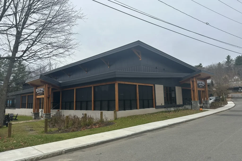 Modern commercial building with dark roof, wood-framed windows, stone base, and landscaped grounds in Northeast setting.