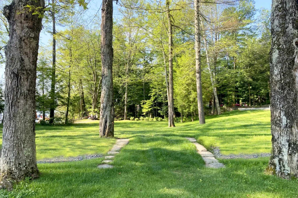 Stone pathways wind through mature trees and green lawn in a Northeast residential landscape design