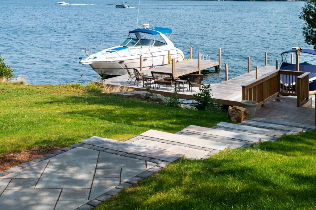 Waterfront residential landscape with stone pathway, lawn, dock, and moored boat showcasing site design.