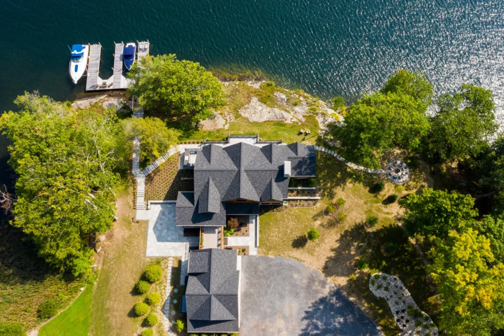 Aerial view of waterfront residence with rocky shoreline, dock, and integrated landscape design on Northeast waterfront