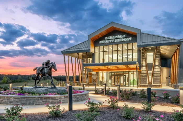 Saratoga County Airport terminal building at dusk with equestrian statue and landscaped grounds featuring pink flowers