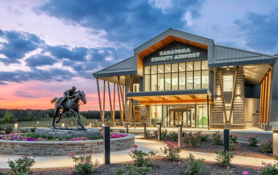 Saratoga County Airport terminal building at dusk with equestrian statue and landscaped grounds featuring pink flowers