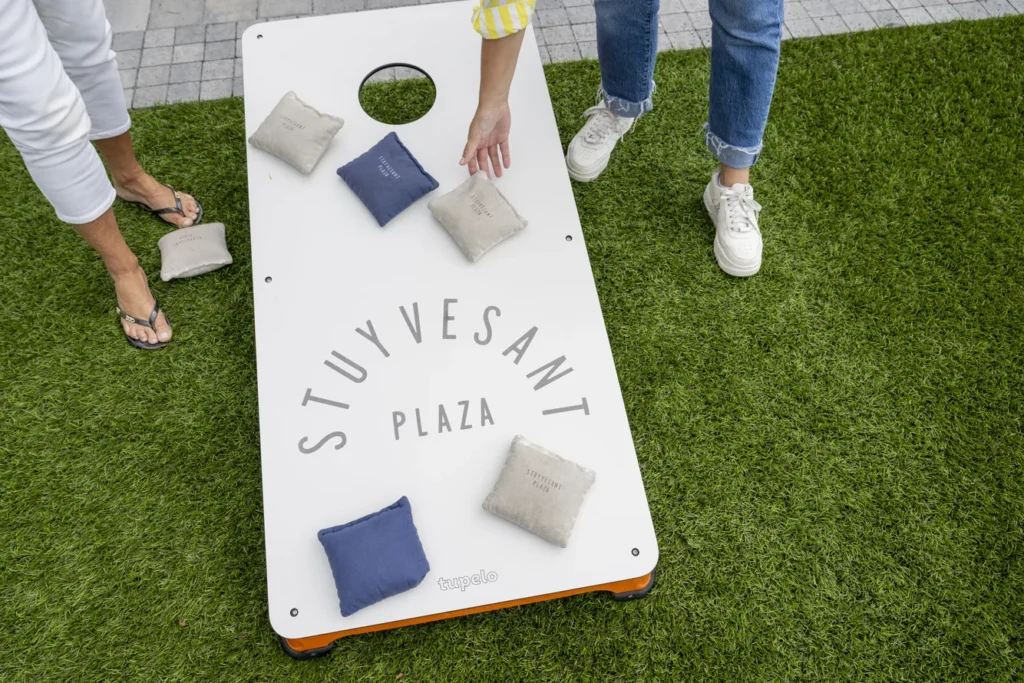 People playing cornhole on artificial turf at Stuyvesant Plaza, a designed outdoor community gathering space