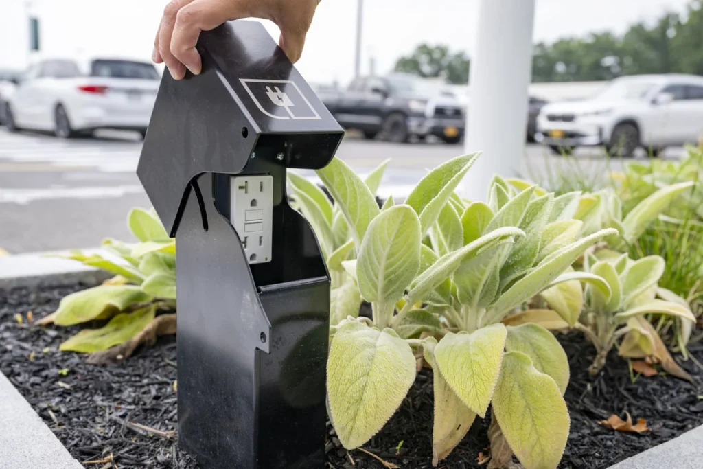 Solar-powered landscape outlet in parking lot planter with green foliage, demonstrating sustainable site design