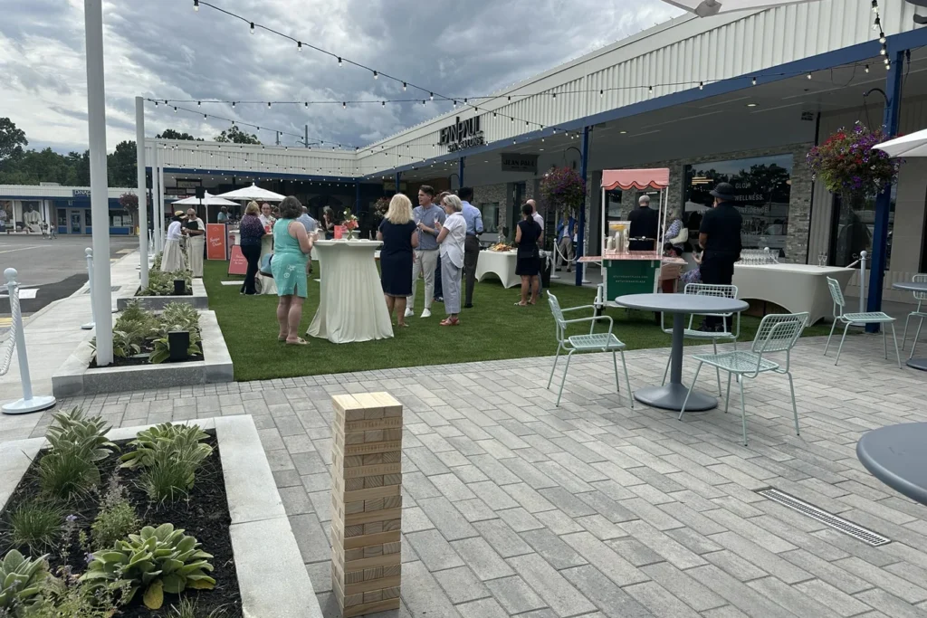 Outdoor plaza event with turf seating area, paved hardscape, and retail storefronts showcasing site design and placemaking