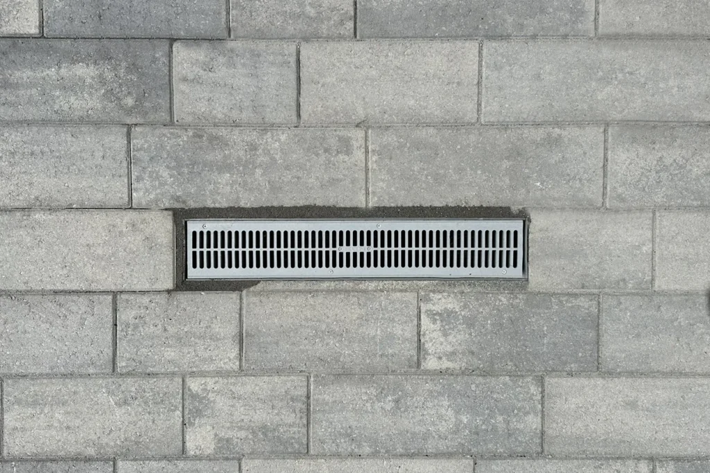 Linear metal drainage grate integrated into concrete paver site design for stormwater management