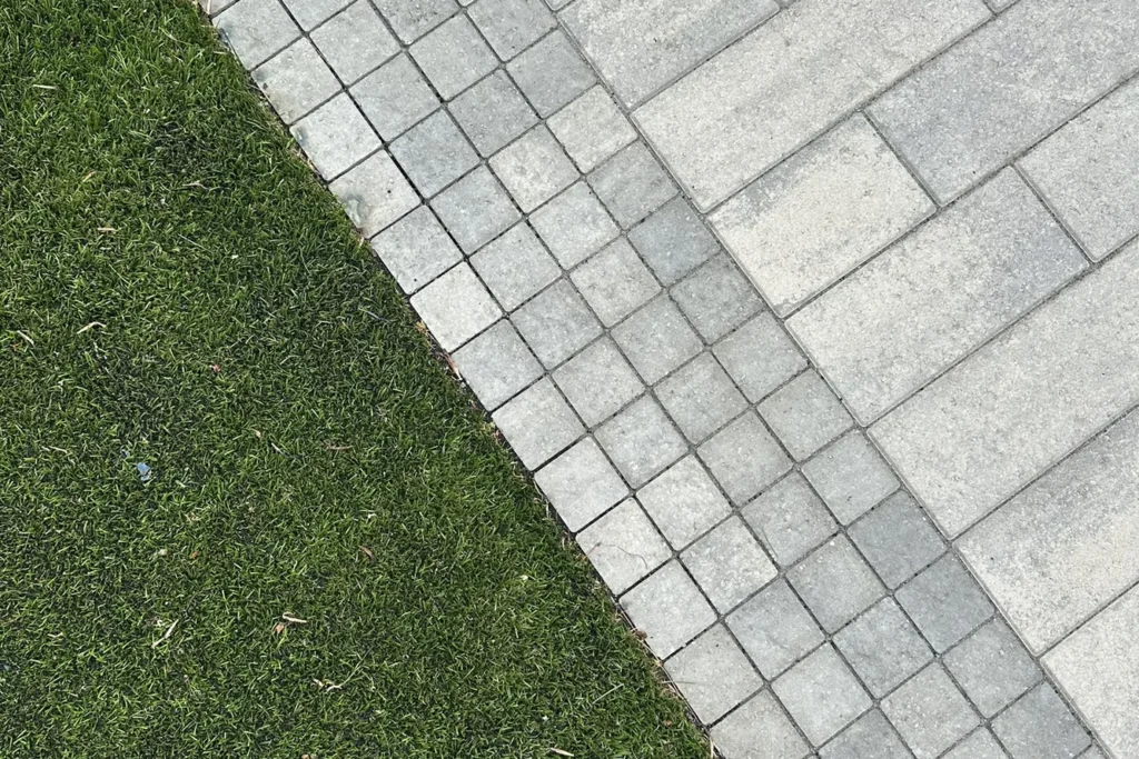 Paved patio with diagonal herringbone pattern meeting manicured lawn edge in landscape site design