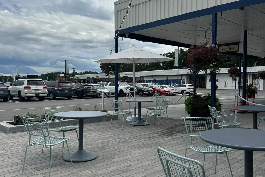 Outdoor plaza seating with umbrellas and tables overlooking parking lot and retail storefronts in site design