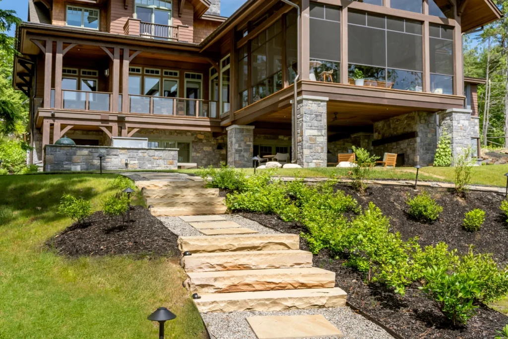 Flagstone steps and landscape planting lead to modern home with stone base and wood detailing overlooking lawn
