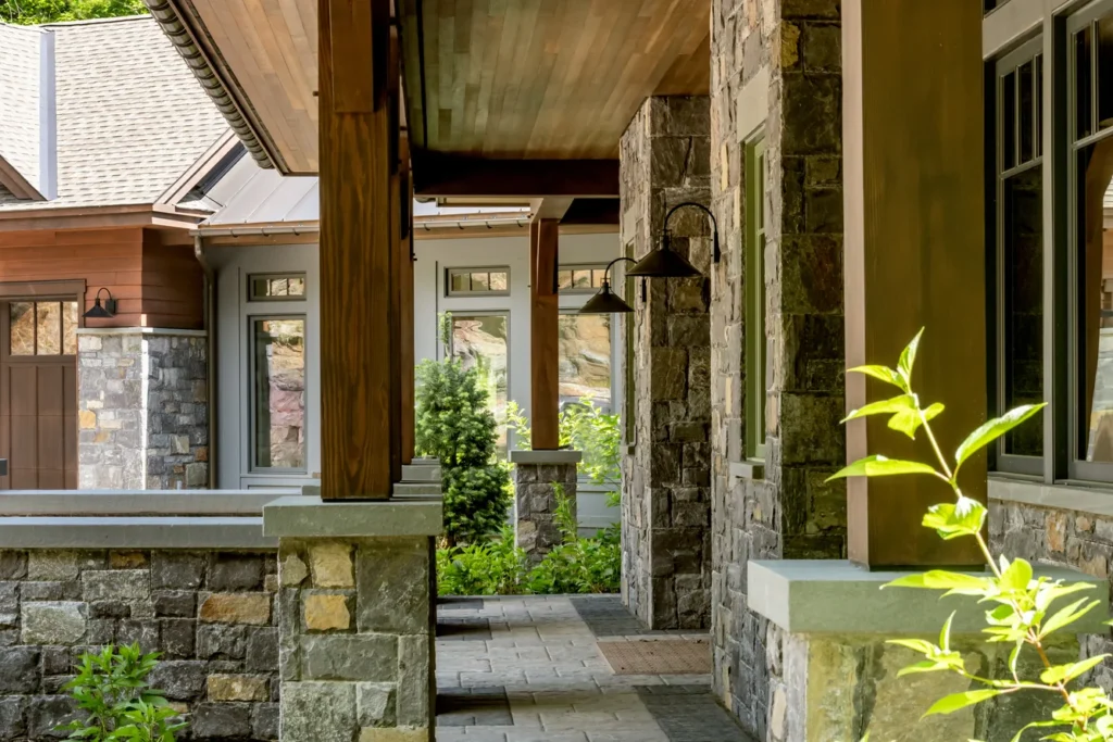Covered stone patio with metal columns, planters, and lush greenery framing contemporary residential architecture