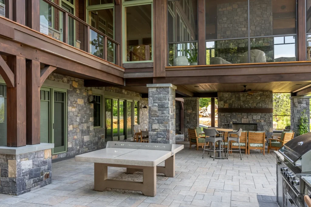 Modern stone patio with integrated outdoor kitchen and seating area under covered structure with wood beams.