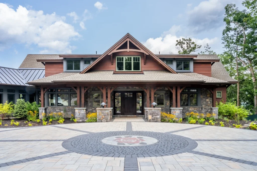 Modern home with stone and timber facade, circular paver entry featuring geometric pattern, and landscaped plantings