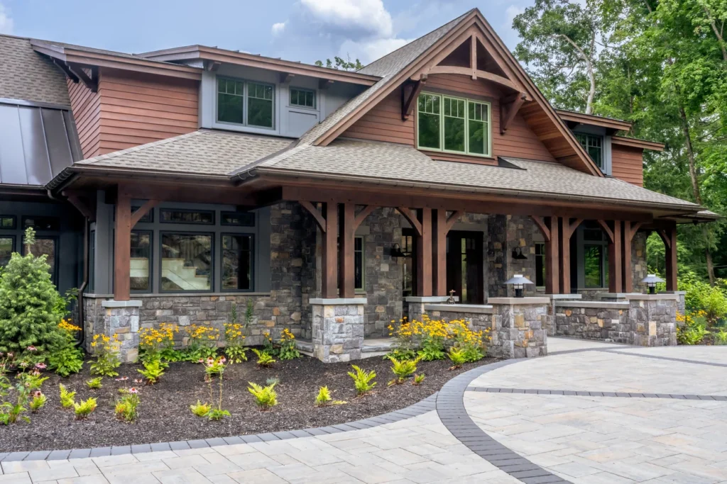 Modern home with stone foundation, paved curved walkway, and landscaped planting beds with yellow flowers and shrubs