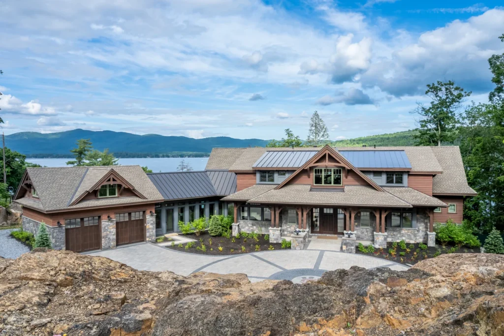 Modern residential home with lakeside views, stone and wood siding, metal roof, and terraced landscape design overlooking