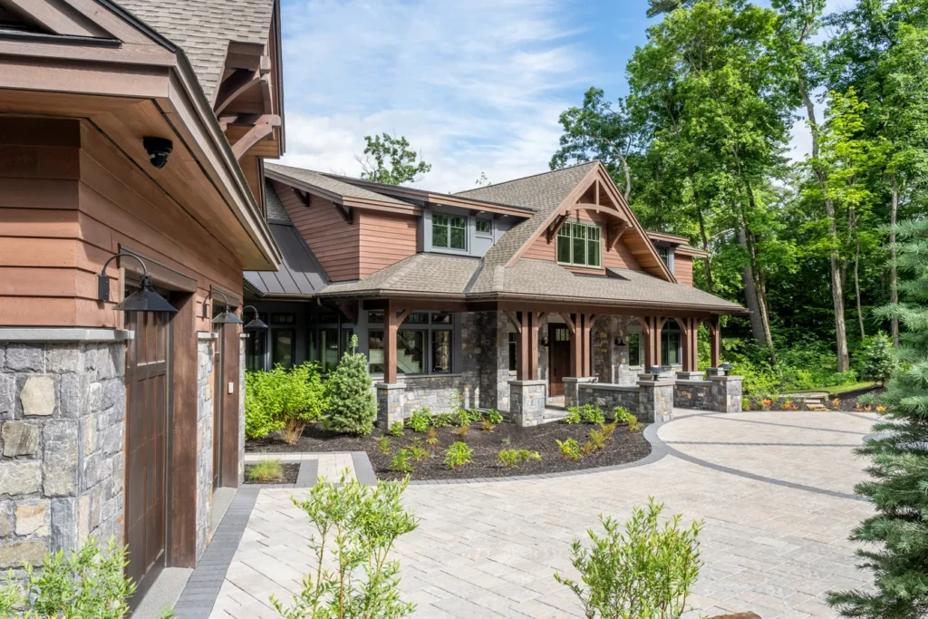 Modern home with stone foundation, manicured landscape beds, and paver driveway surrounded by mature trees