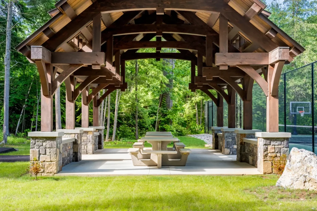 Timber post pavilion with stone pillars and picnic tables in wooded landscape site design setting