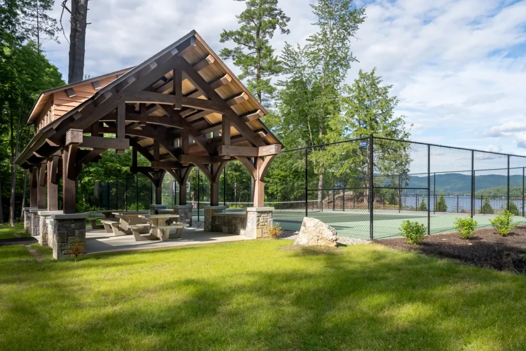 Timber pavilion with stone fireplace overlooking lake and tennis court in landscape design setting