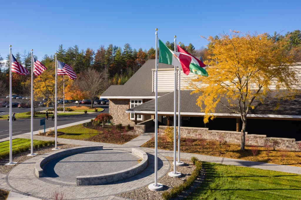 Modern campus entry with curved paver plaza, flagpoles, and autumn landscaping in Northeast setting