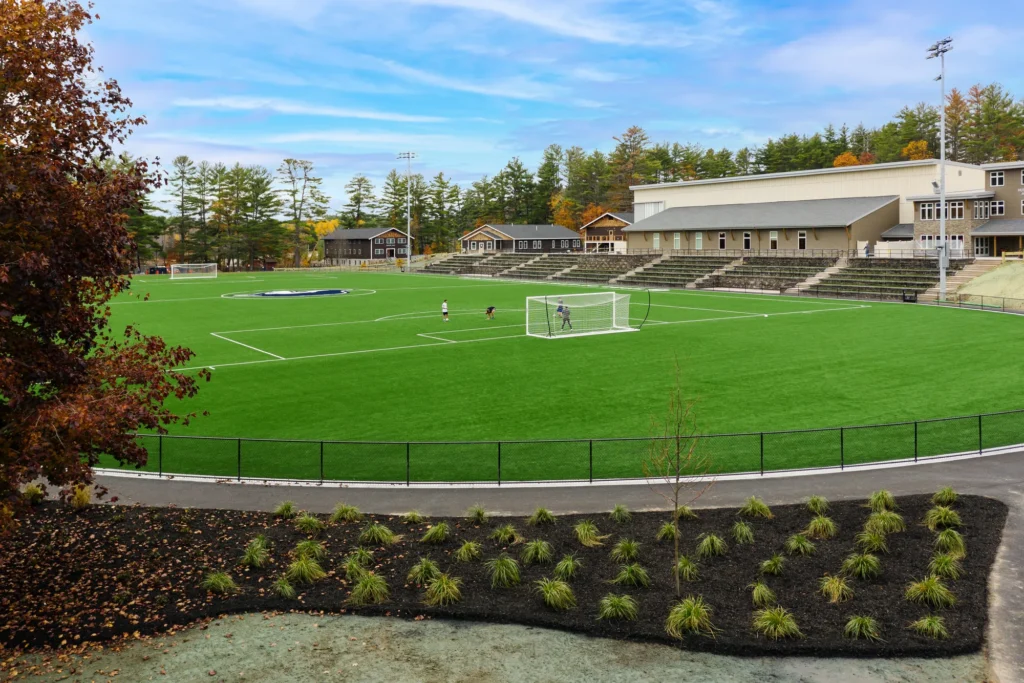 Athletic field with terraced seating, ornamental plantings, and modern site design for a Northeast campus facility.